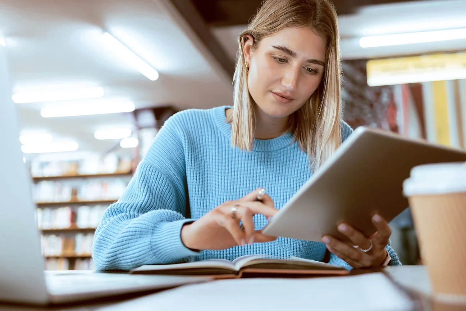 A woman sitting indoors, using a tablet in a classroom setting.