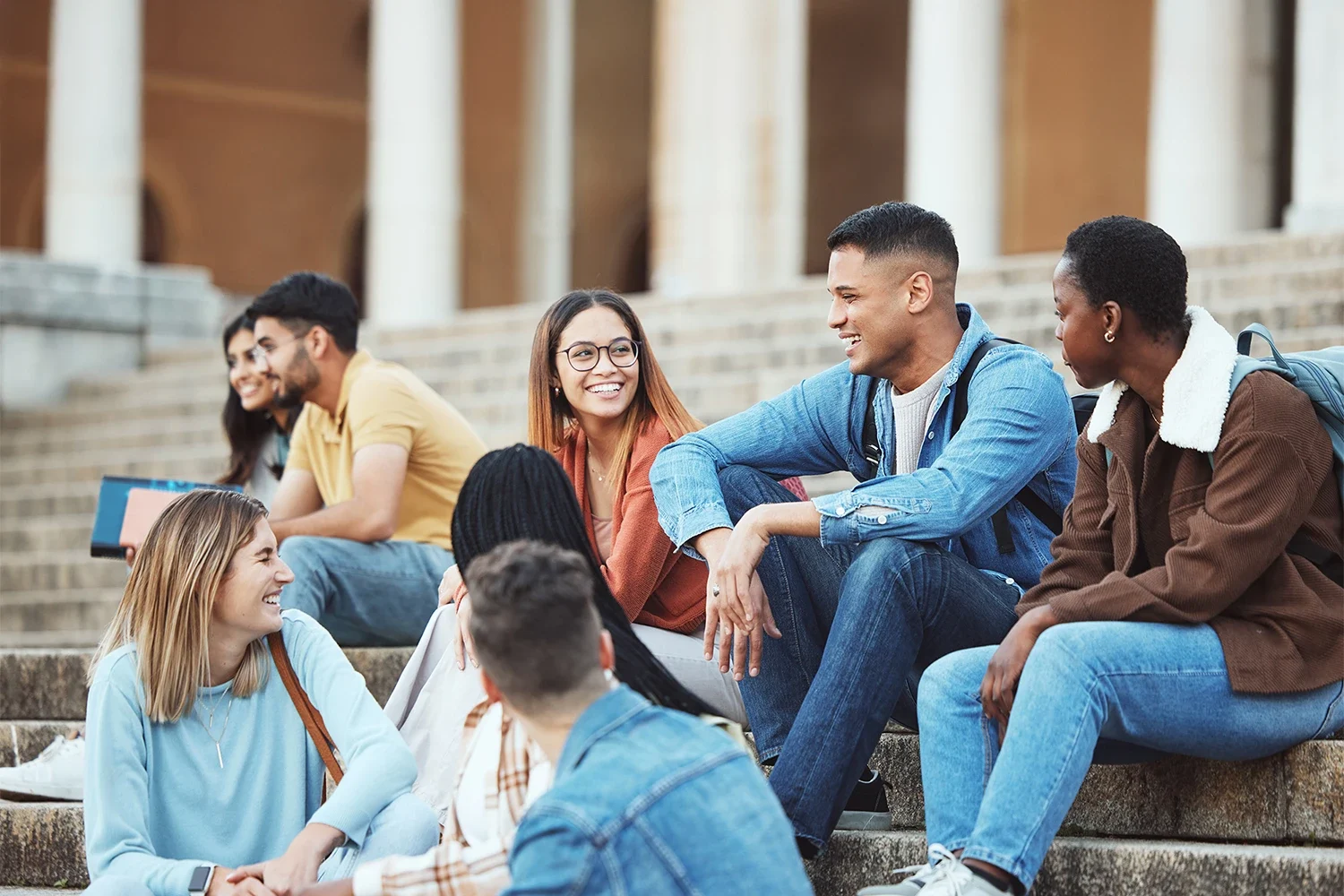 Several students sitting in an outdoor staircase talking and smiling.