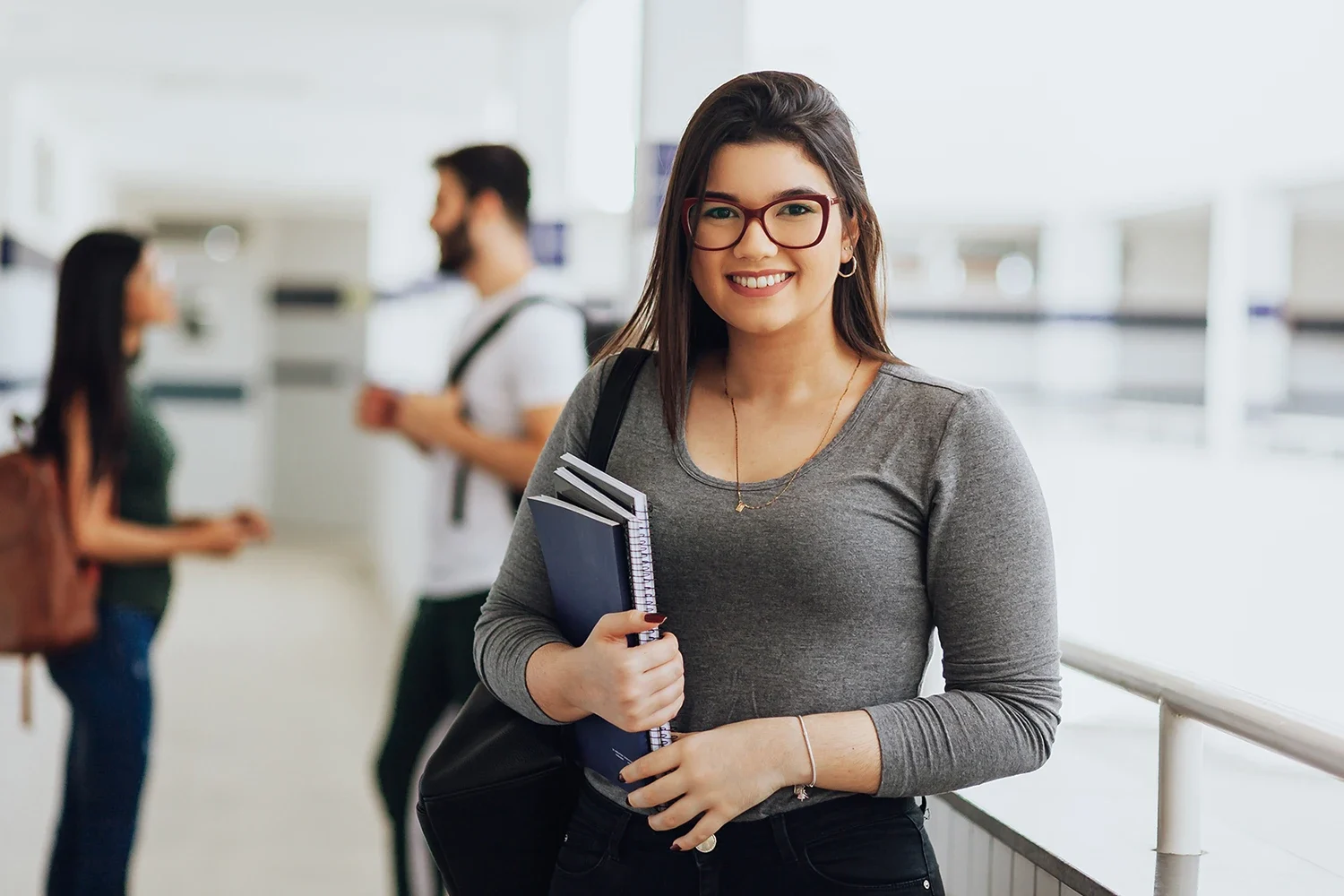 A woman holding notebooks looking and smiling at the camera in a school setting